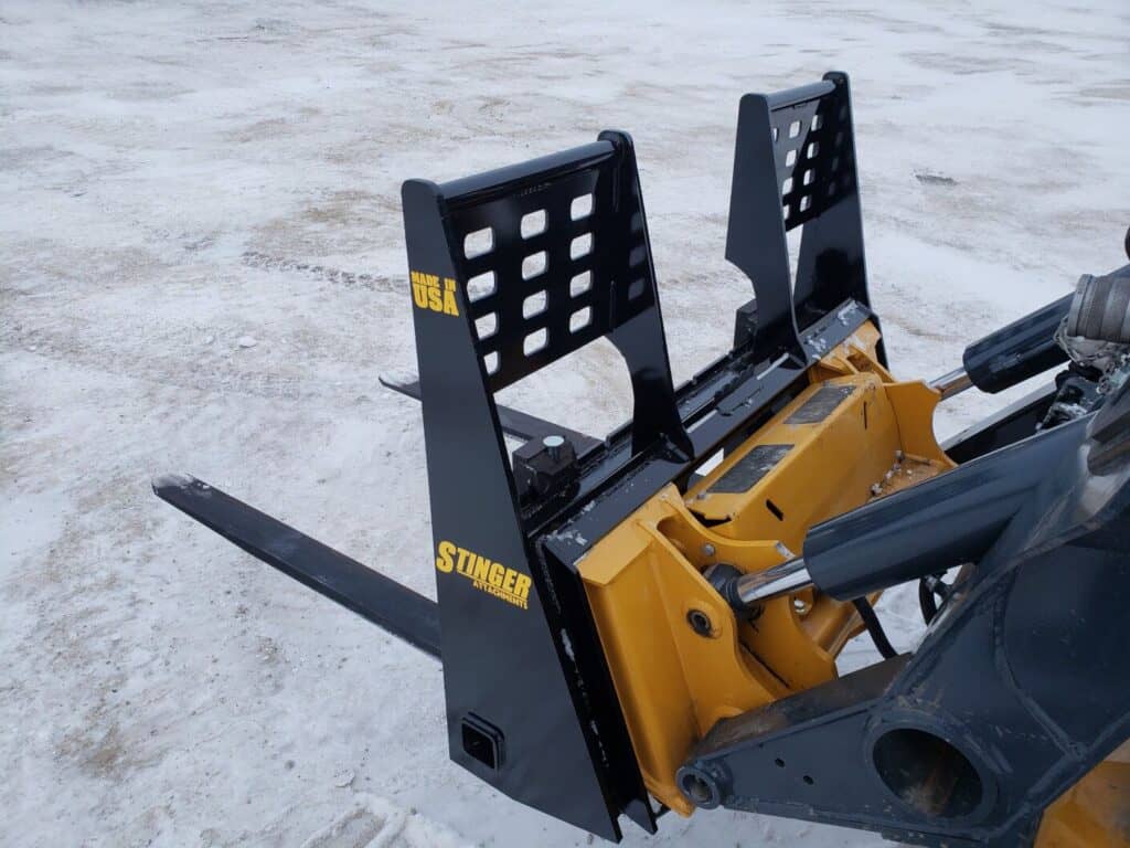 Stinger skid steer pallet fork attachment mounted on skid steer loader for lifting pallets and job site materials