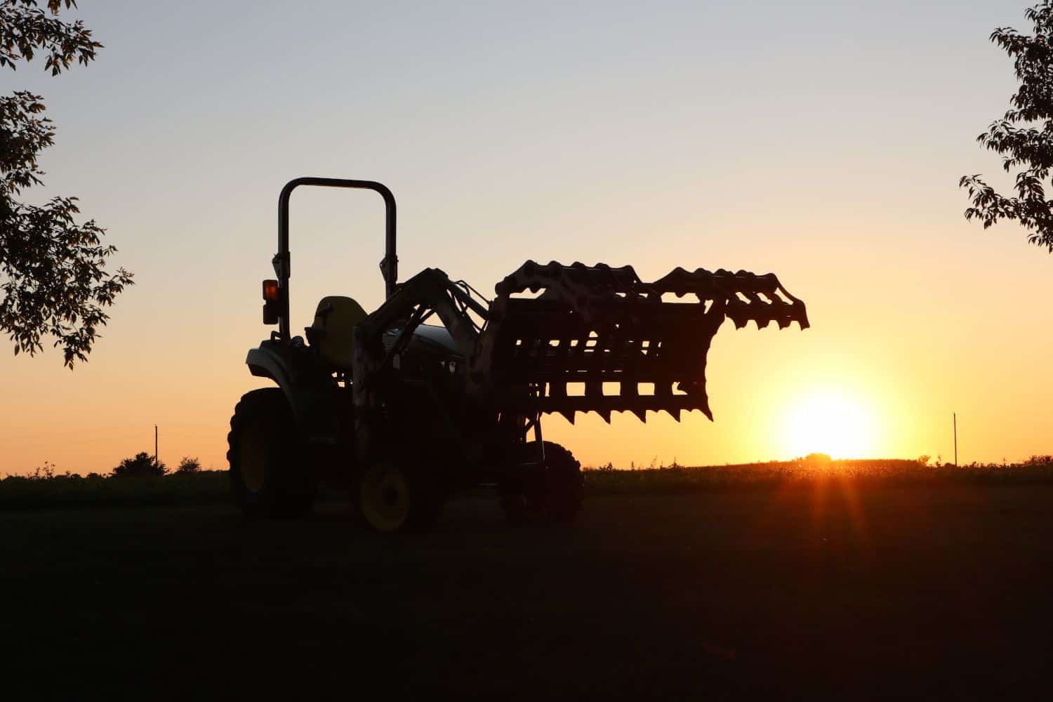 Silhouette of compact tractor using Stinger CCG grapple attachment during sunset land clearing work