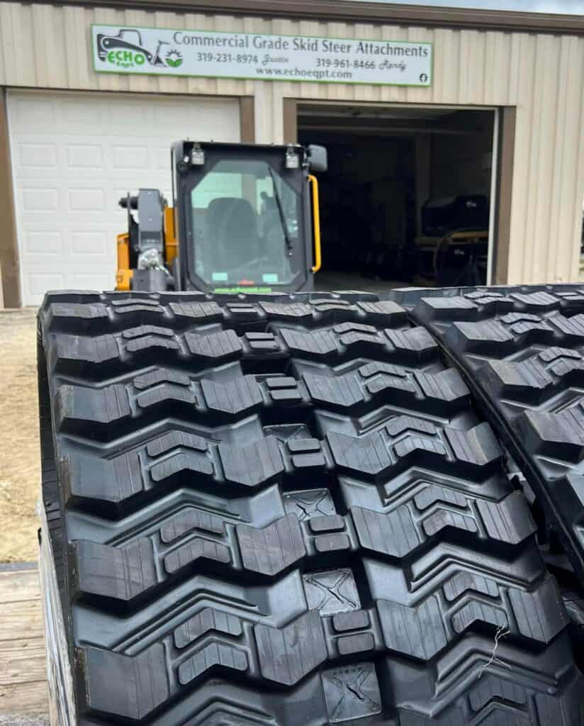 Skid steer loader equipped with heavy duty rubber tracks parked outside equipment dealership building