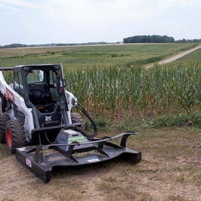 Prime Attachments rigid deck skid steer brush mower clearing field vegetation along edge of agricultural crop field