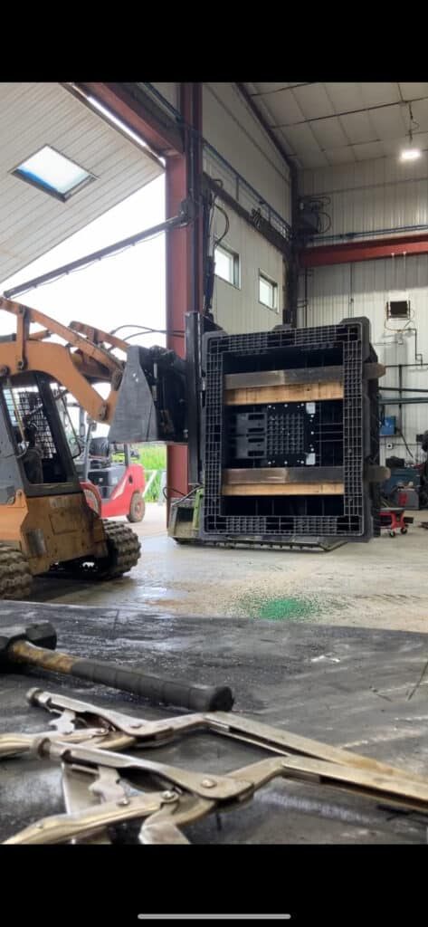ECHO PF180 skid steer box flipper attachment side view lifting and rotating large crate inside warehouse