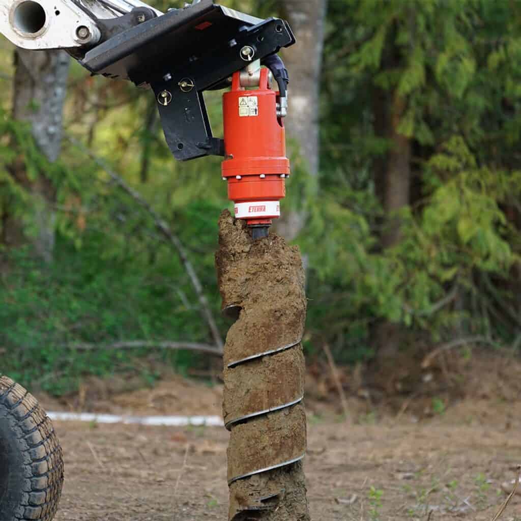 Skid steer auger attachment drilling holes in soil using Eterra auger drive