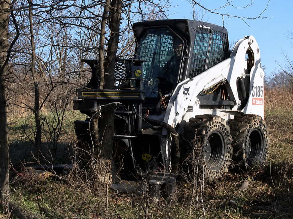 M&M Hydra Clip 16 inch grapple tree shear attached to Bobcat skid steer in wooded area