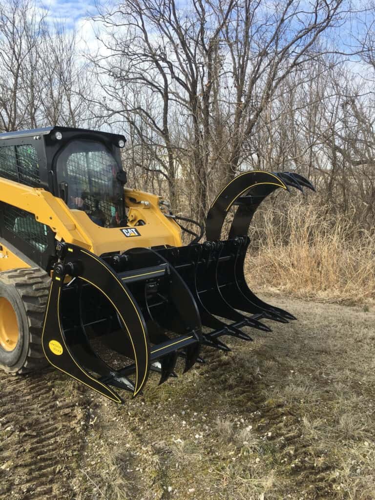 M&M Hydra Rake Extreme grapple rake attachment mounted on skid steer in woods