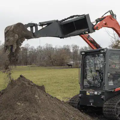 Prime Attachments skid steer backhoe loading dirt into bucket showing material handling and digging capability
