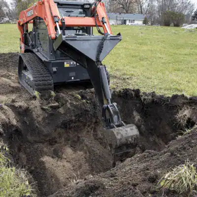 Prime Attachments skid steer backhoe mounted on track loader digging soil showing trenching and excavation performance