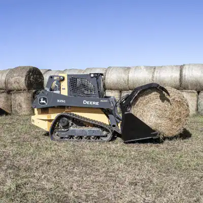 Prime Attachments high capacity skid steer grapple lifting round hay bale in agricultural field setting