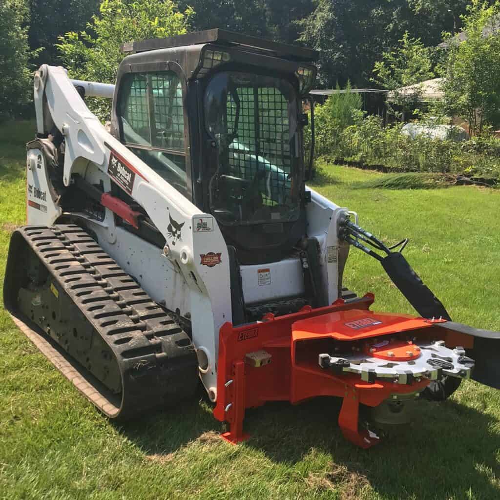 Eterra Vortex skid steer stump grinder attachment operating on Bobcat skid steer removing tree stump in wooded property