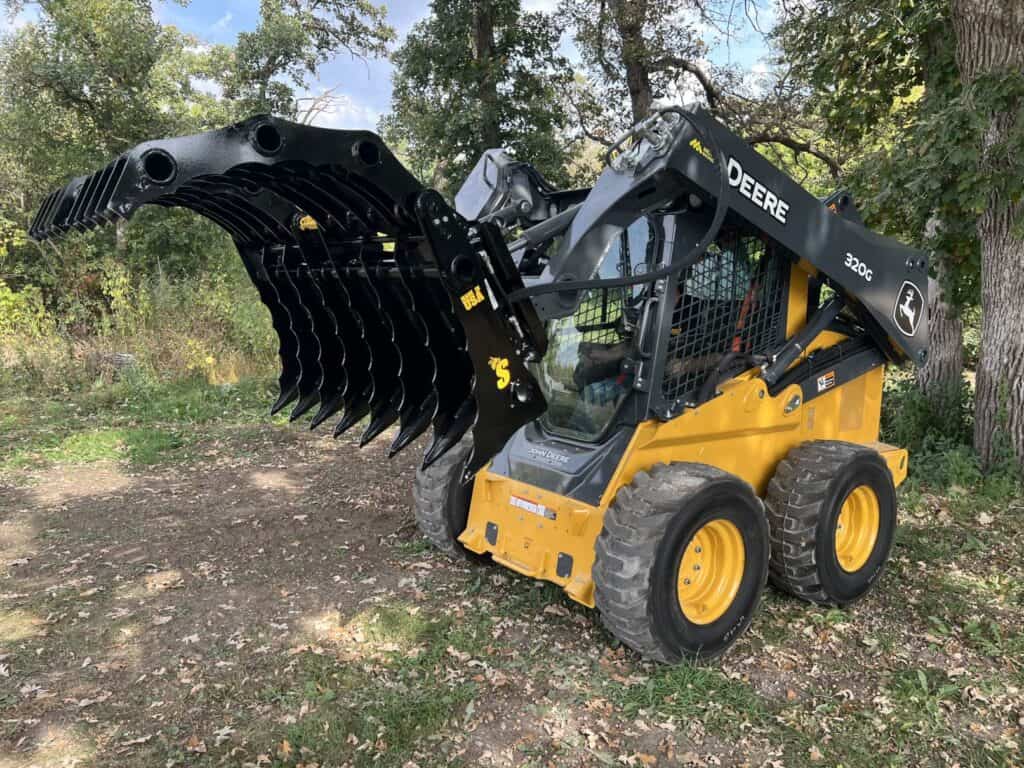 Stinger CC skid steer clam grapple mounted on skid steer clearing brush in wooded area showing real world performance