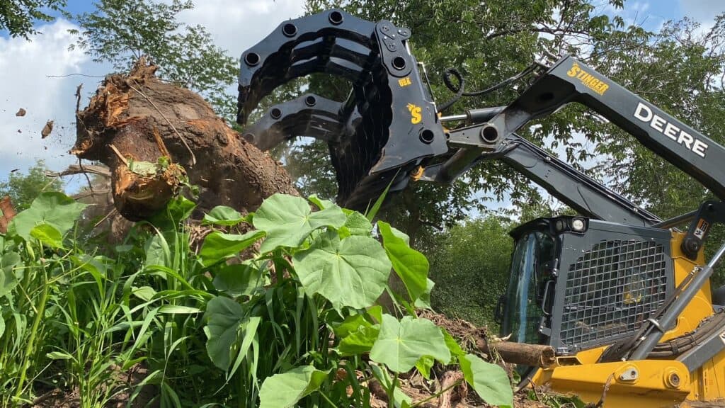 Stinger skid steer root grapple attachment grabbing tree debris during land clearing work