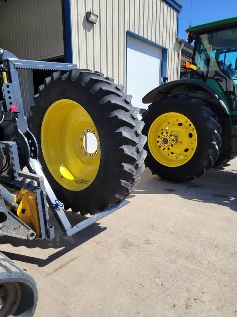 Large John Deere tractor tire positioned near ECHO OG skid steer tire handler attachment