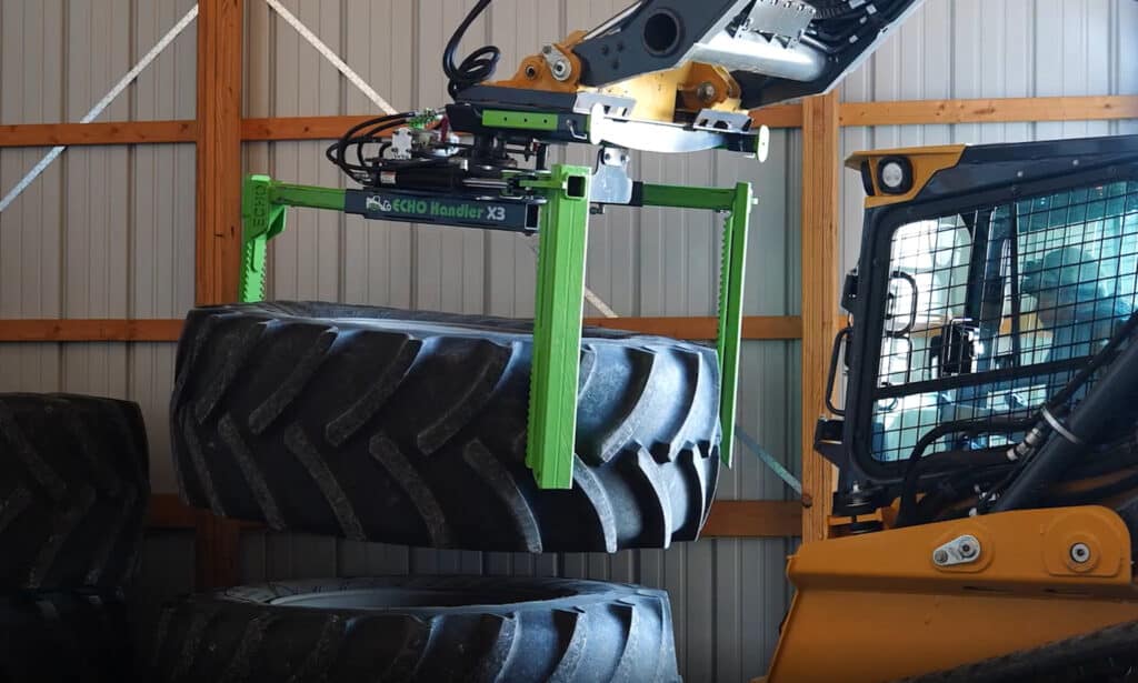 ECHO Handler X3 skid steer tire handler stacking a large agricultural tire inside a farm equipment shop