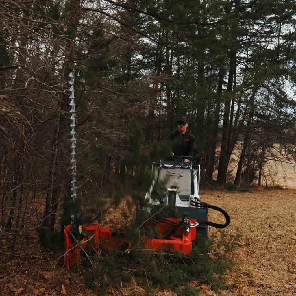 Eterra mini skid steer sickle bar mower in operation cutting brush and small trees in wooded area
