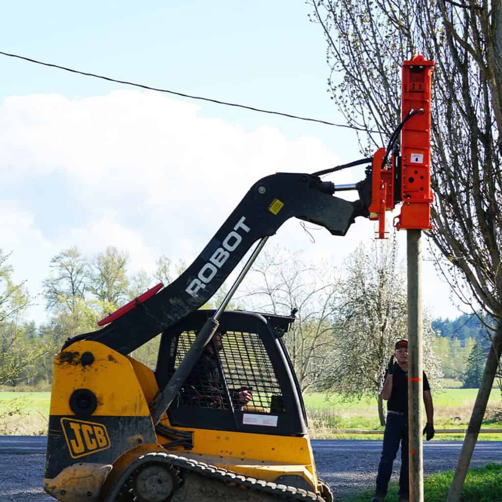 Eterra PDX-1000 skid steer post driver attachment installing wooden fence post with hydraulic hammer and grapple clamp