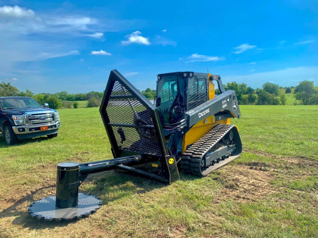 M&M Hydra Saw attachment mounted on John Deere 331G skid steer in grassy field