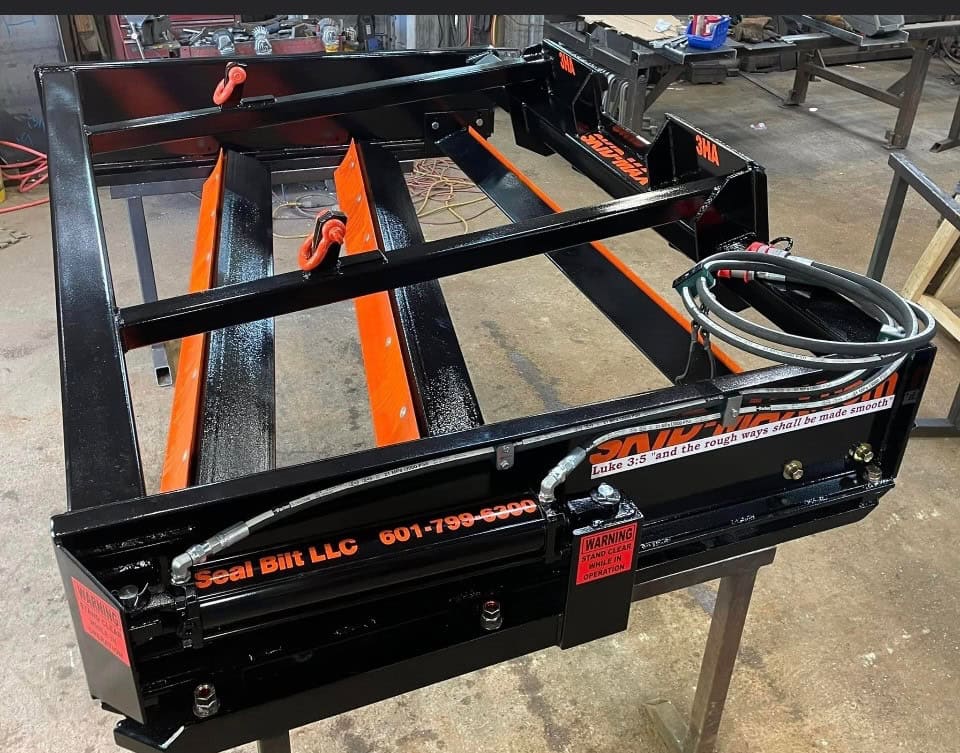 Orange Skid Max 3 blade hydraulic skid steer grader attachment in workshop close up