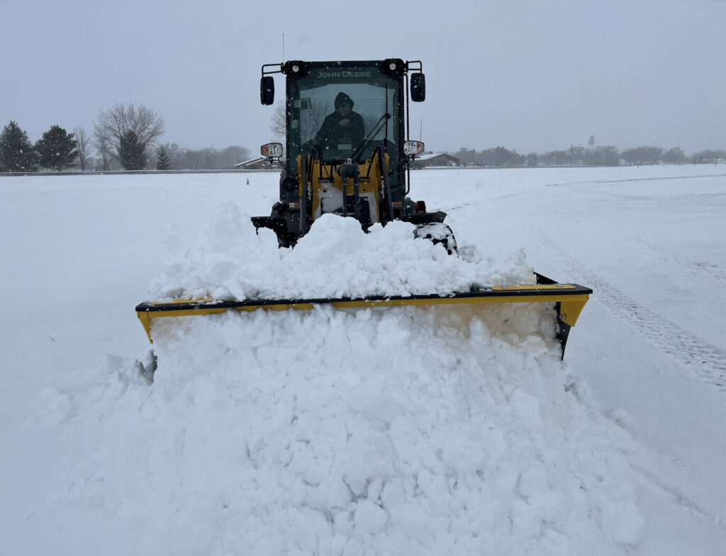 Front view of Stinger SPX8 snow pusher clearing deep snow with a John Deere wheel loader