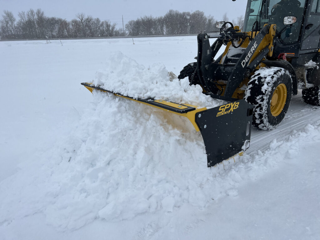 Stinger SPX8 snow pusher moving deep packed snow with a John Deere wheel loader