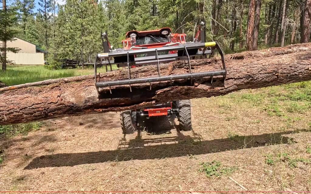 Front view of an ANBO CLASP-IT mechanical grapple securely carrying a long log with a compact tractor