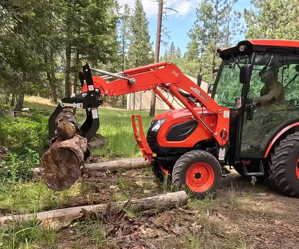 Kioti compact tractor using an ANBO CLASP-IT mechanical grapple to lift a large log in a wooded area
