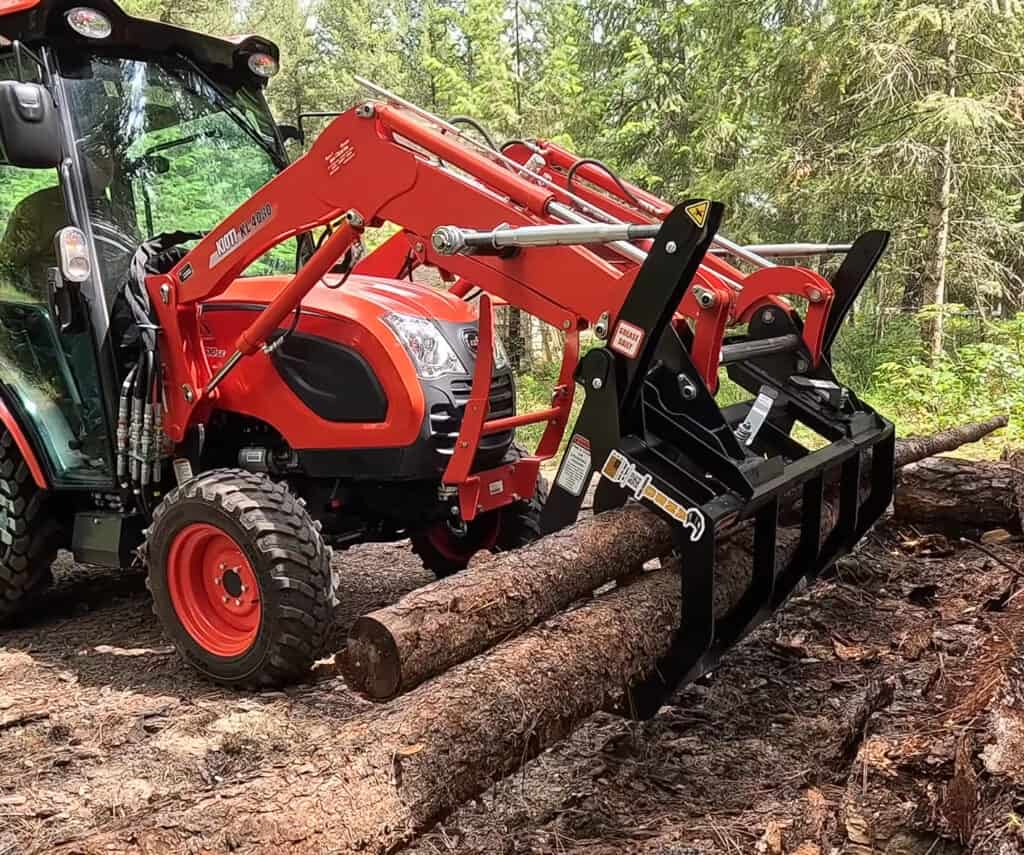 ANBO CLASP-IT mechanical grapple on a Kioti compact tractor positioned over several logs during property cleanup