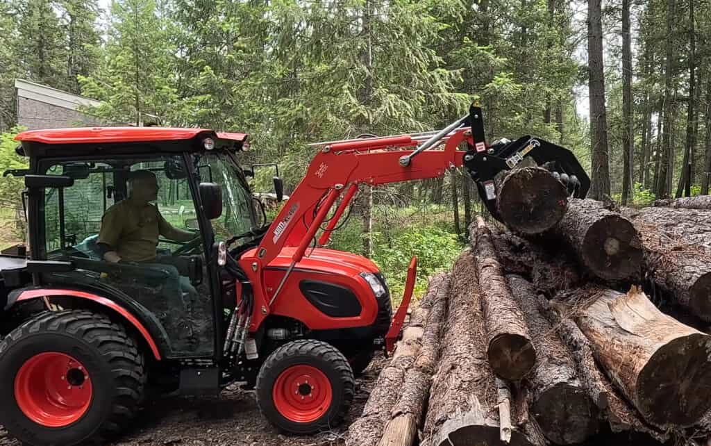 ANBO CLASP-IT mechanical grapple on a Kioti compact tractor lifting a log from a wooded log pile