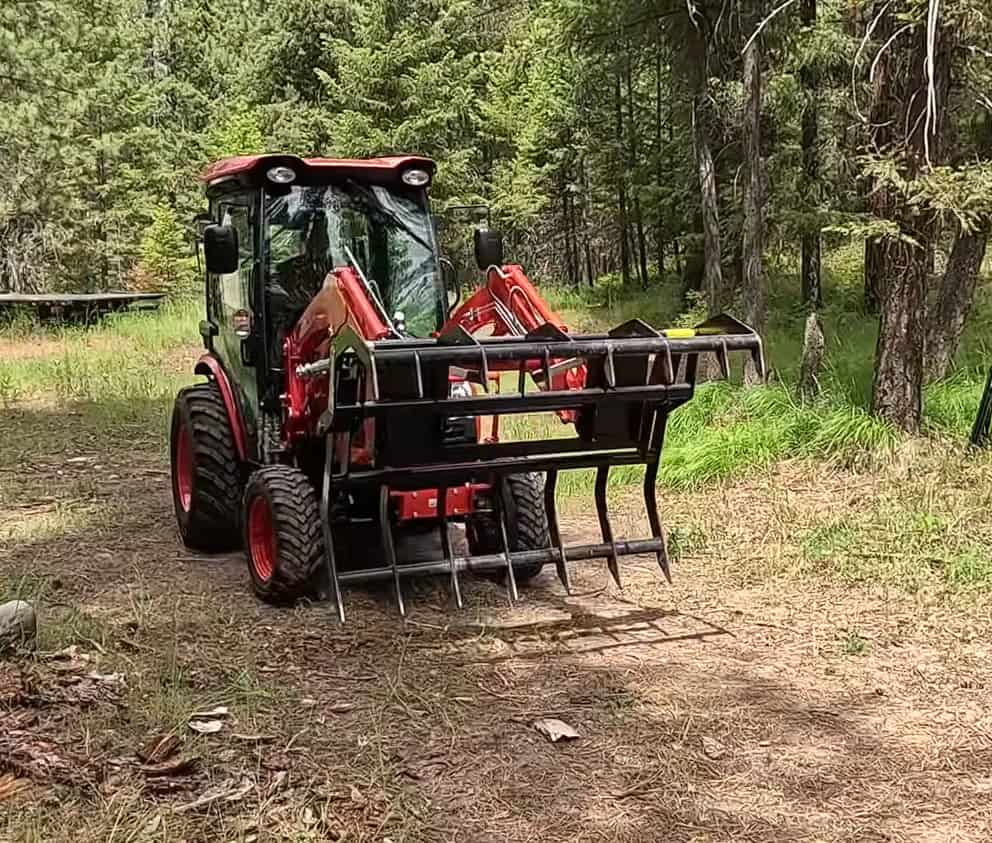 Open ANBO CLASP-IT mechanical grapple shown from the front on a Kioti compact tractor in a wooded work area