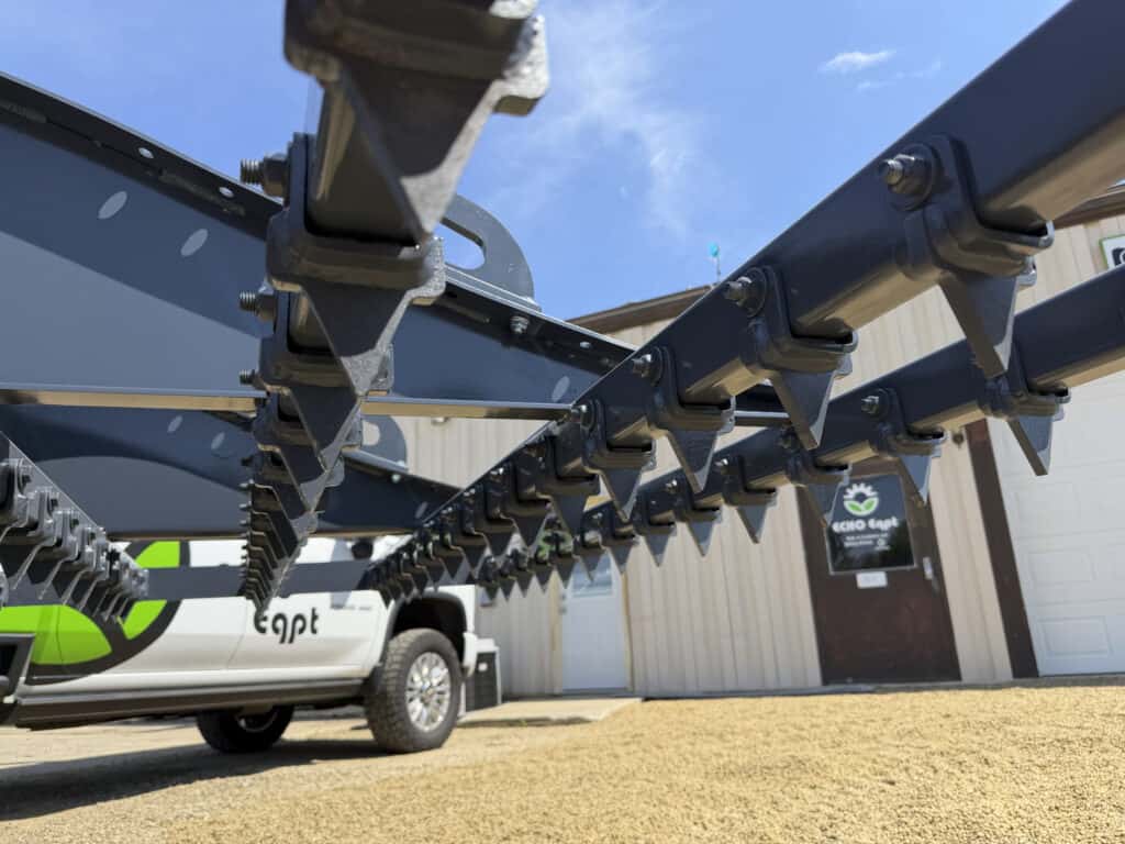 Underside view of the ECHO 92 inch skid steer drag landscape rake showing multiple rows of aggressive steel teeth