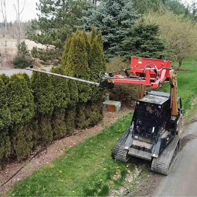 ASV compact track loader using an Eterra skid steer sickle bar mower to trim the top of a tall hedge