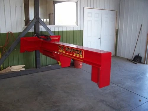 TM Manufacturing HD skid steer log splitter shown indoors with the hydraulic beam and fixed splitting wedge
