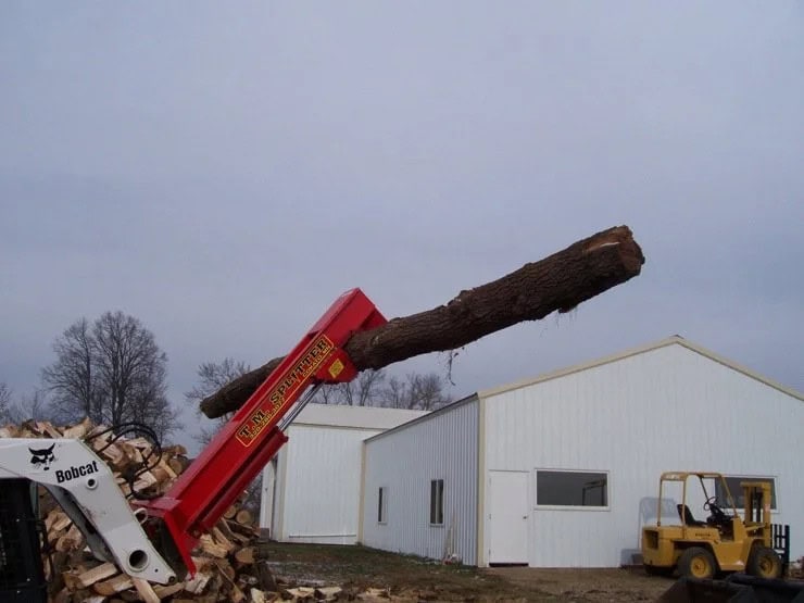 TM Manufacturing Pro 1 skid steer log splitter moving a long log across a wood processing yard