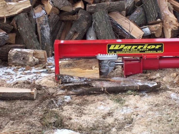 Close-up of the TM Manufacturing Warrior skid steer log splitter working beside a large pile of firewood