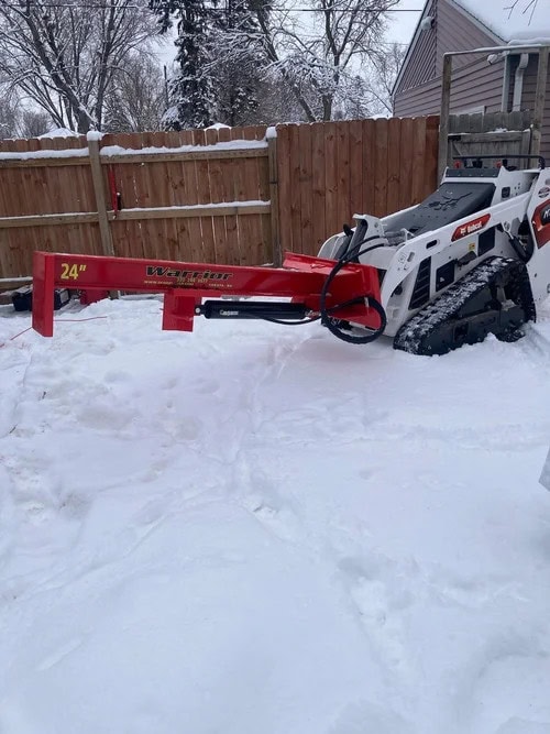 TM Manufacturing Warrior Mini 24 inch log splitter attached to a Bobcat MT100 mini track loader in a snow-covered yard