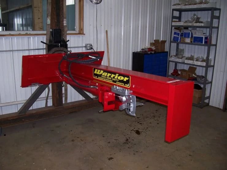 TM Manufacturing Warrior skid steer log splitter indoors showing the hydraulic beam, hoses and splitting mechanism