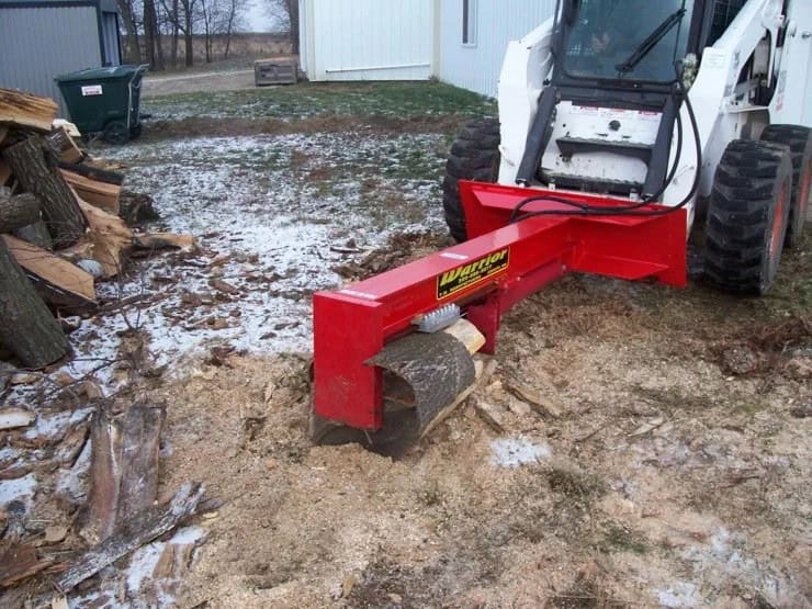 TM Manufacturing Warrior skid steer log splitter splitting a log on the ground in a snowy wood processing area