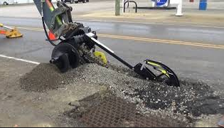 Digga Bigfoot 1200 skid steer trencher cutting through pavement during utility and roadwork