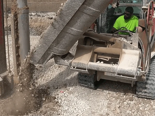 Maxx Attachments Side Dump Bucket unloading gravel in a confined construction area
