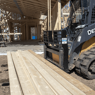 Prime Attachments Skid Steer Pallet Forks carrying stacked lumber on a John Deere compact track loader