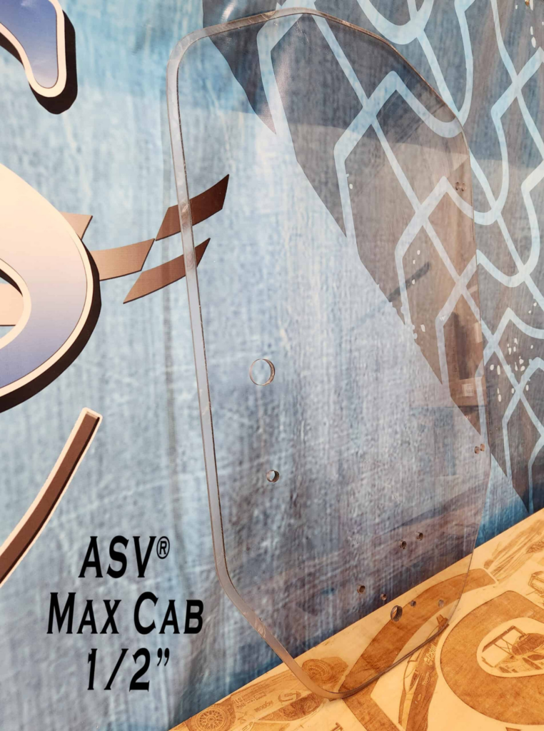 Angled view of SHIELDS ASV Max Cab polycarbonate windshield showing the curved profile and factory-style mounting holes.