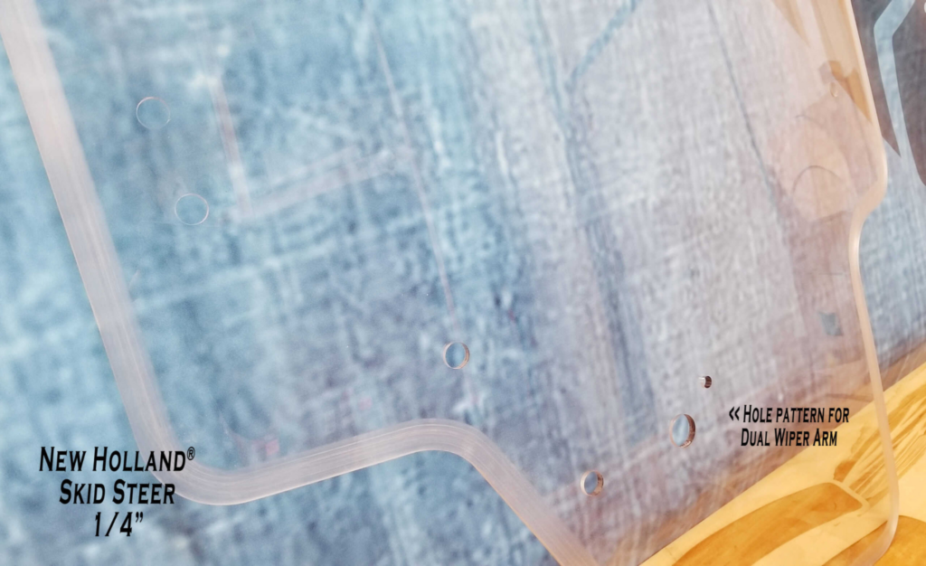 Close-up of the SHIELDS Case and New Holland quarter-inch polycarbonate windshield showing the dual-wiper hole pattern