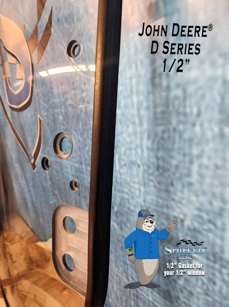 Close-up of the SHIELDS John Deere D and E Series half-inch polycarbonate windshield showing the mounting holes and SHIELDS Seal