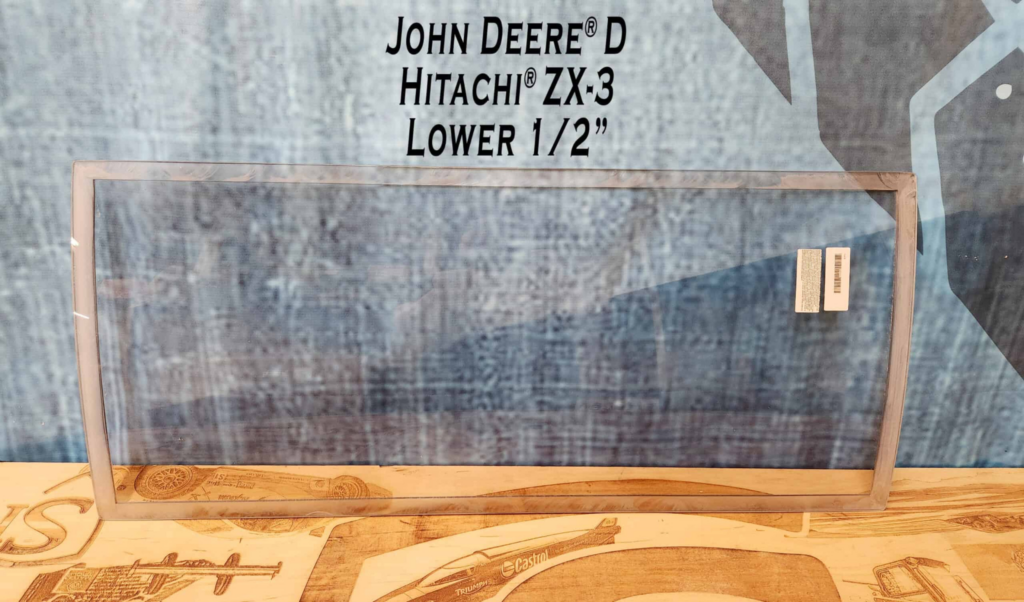 Front view of SHIELDS John Deere D Series polycarbonate lower excavator windshield showing the full curved window shape.