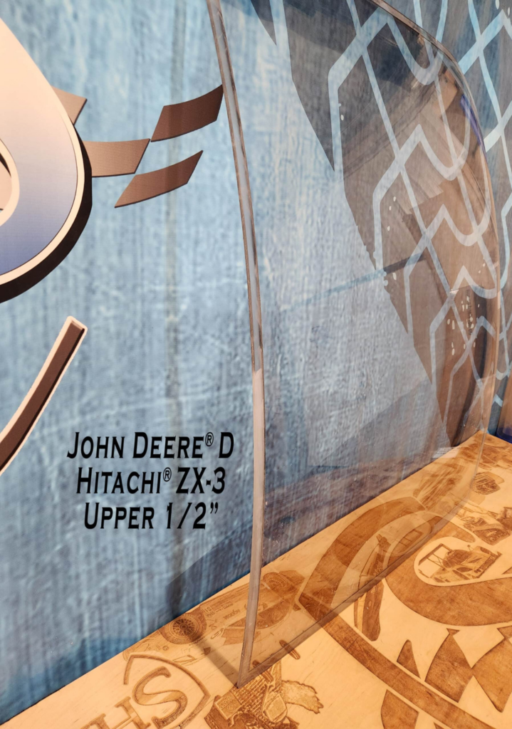 Angled side view of SHIELDS John Deere D Series polycarbonate upper excavator windshield showing its curved profile.