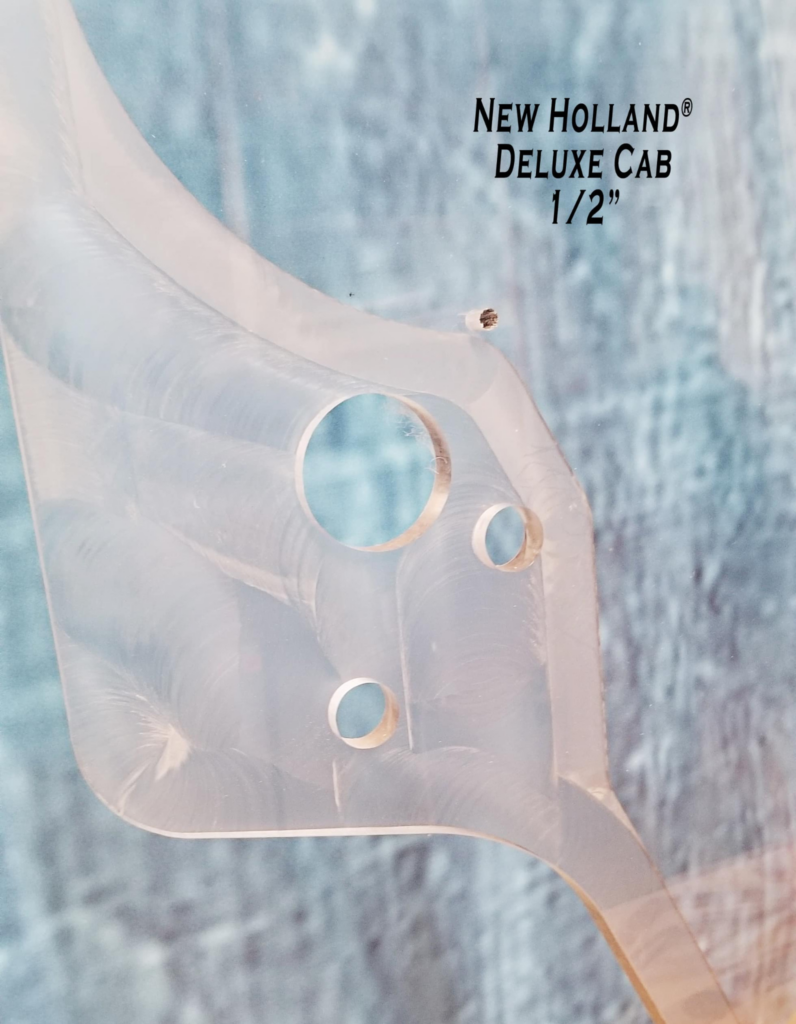 Close-up of SHIELDS New Holland Deluxe Cab polycarbonate windshield showing the precision-machined mounting holes.