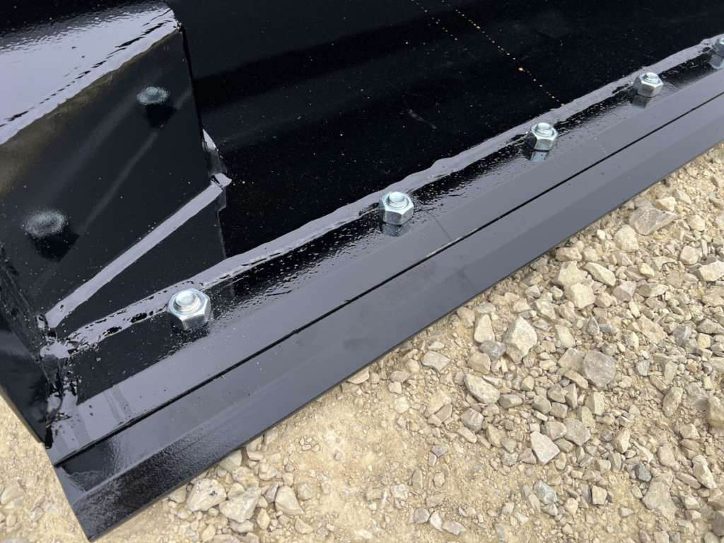 Close-up of the reversible bolt-on cutting edge on the Stinger skid steer hydraulic dump bucket