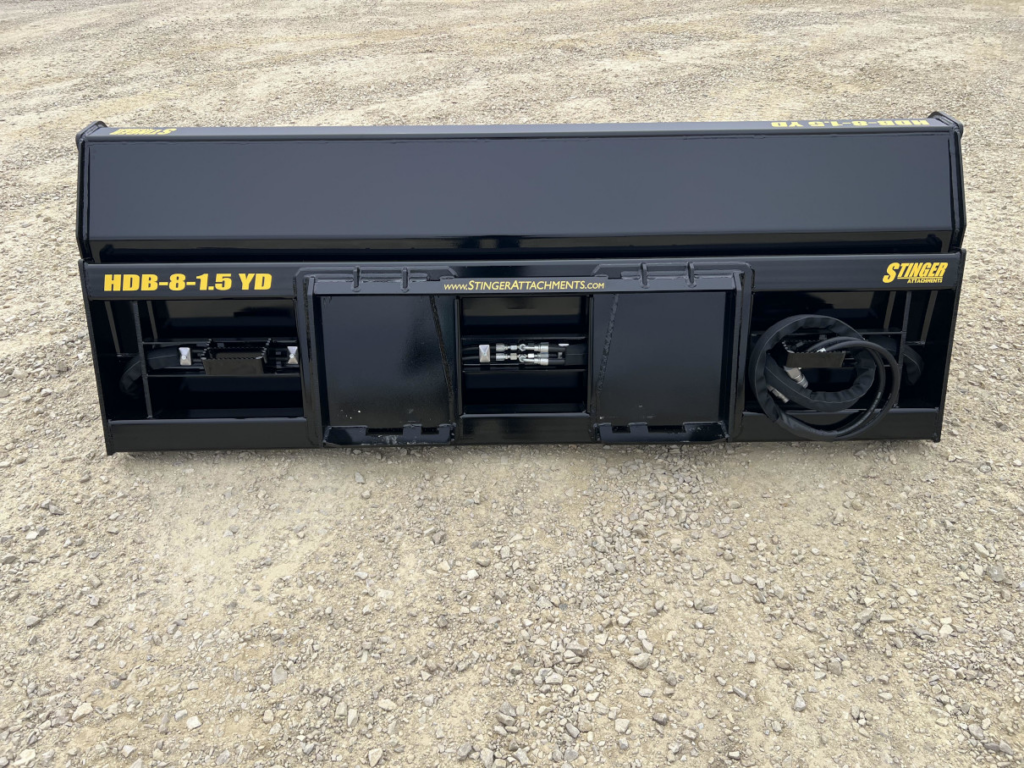 Rear view of the Stinger skid steer hydraulic dump bucket showing the skid steer mount, support frame, and hydraulic hose storage