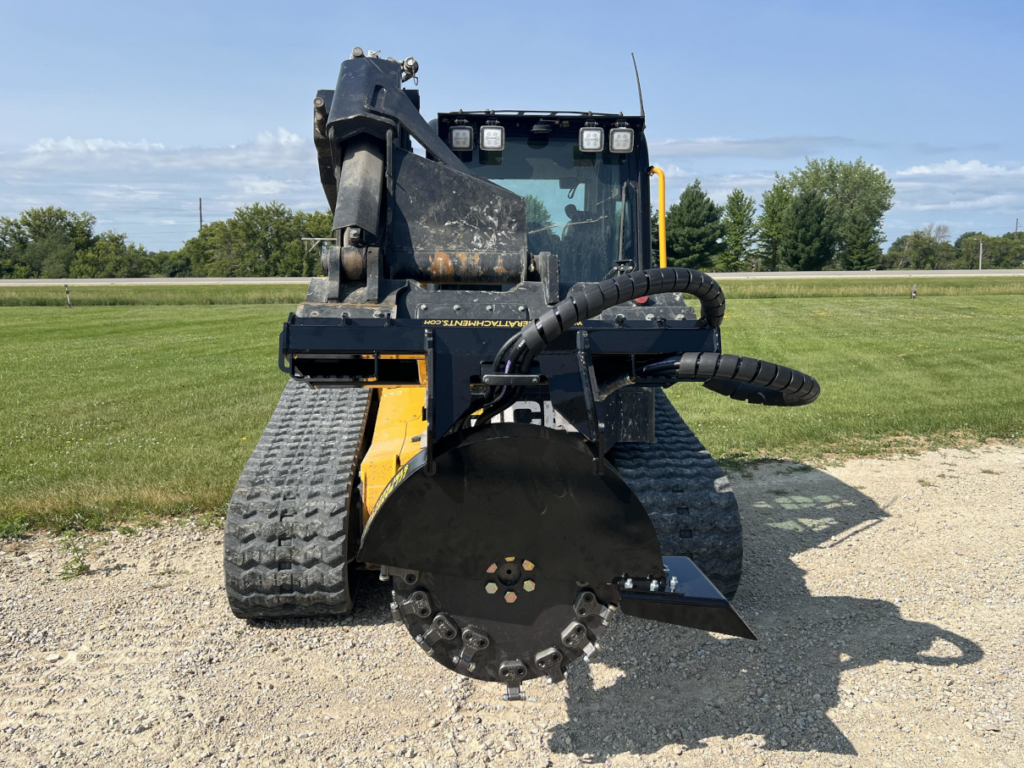 Front view of the Stinger skid steer stump grinder mounted on a compact track loader with the cutting wheel and protective guard visible