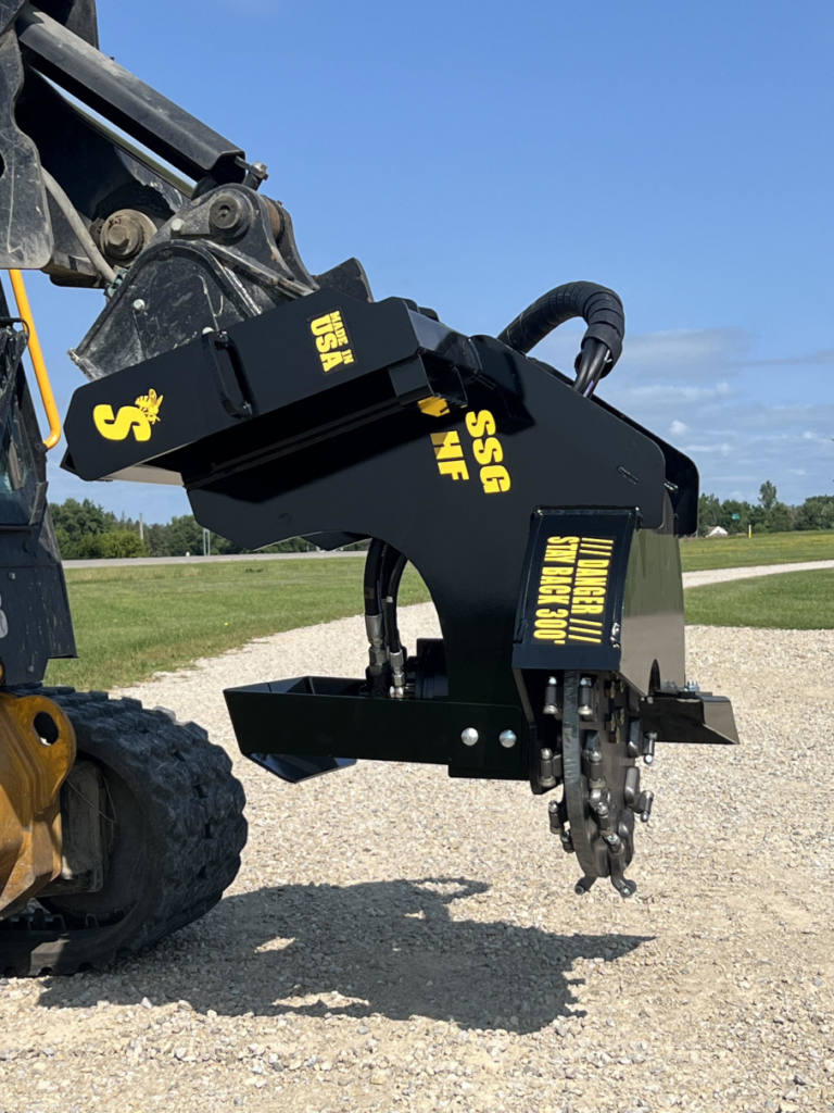 Stinger skid steer stump grinder mounted on a compact track loader, shown from the side with the cutting wheel and hydraulic hose routing