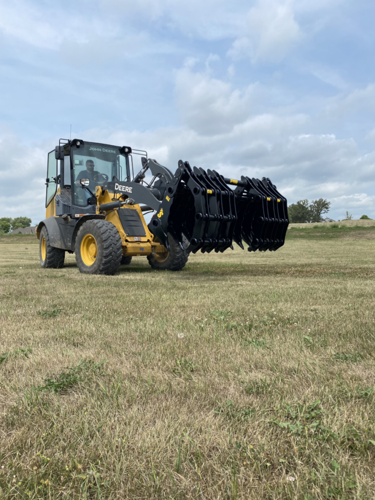 John Deere wheel loader carrying the Stinger Wheel Loader Clam Grapple across a job site