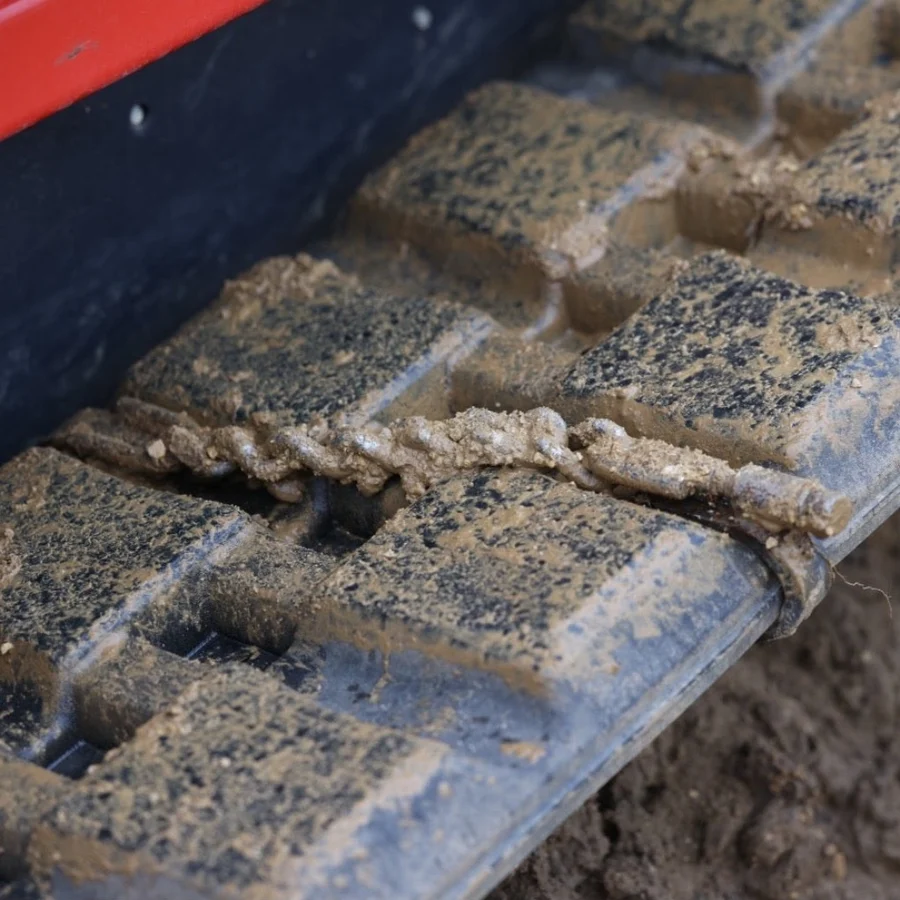 Close-up of a Stout TrackClaws traction chain installed across a muddy rubber track